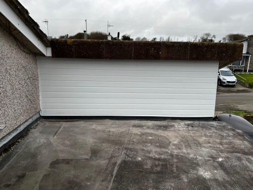 White garage door with a brown roof, situated next to a residential building.