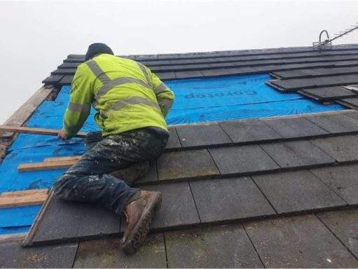 A worker installing roofing tiles on a building under overcast conditions.